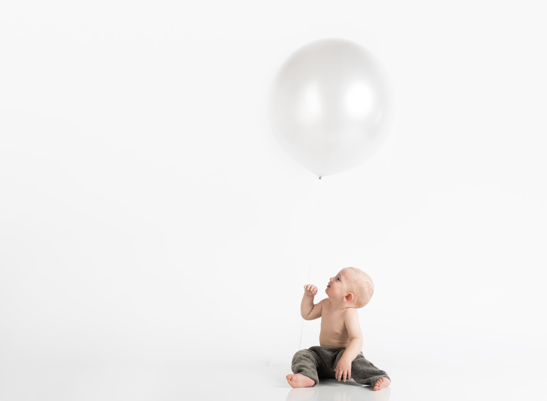 topless toddler with pants sitting on white surface while looking up